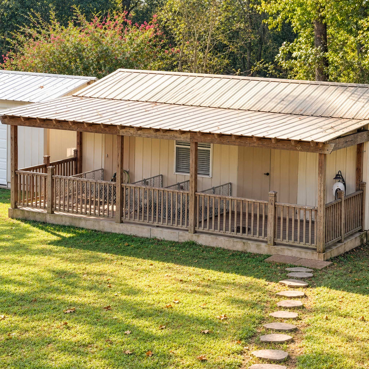 A rustic wooden cabin with a metal roof, elevated porch with railings, and a stone path leading up to it on a grassy lawn with trees in the background.
